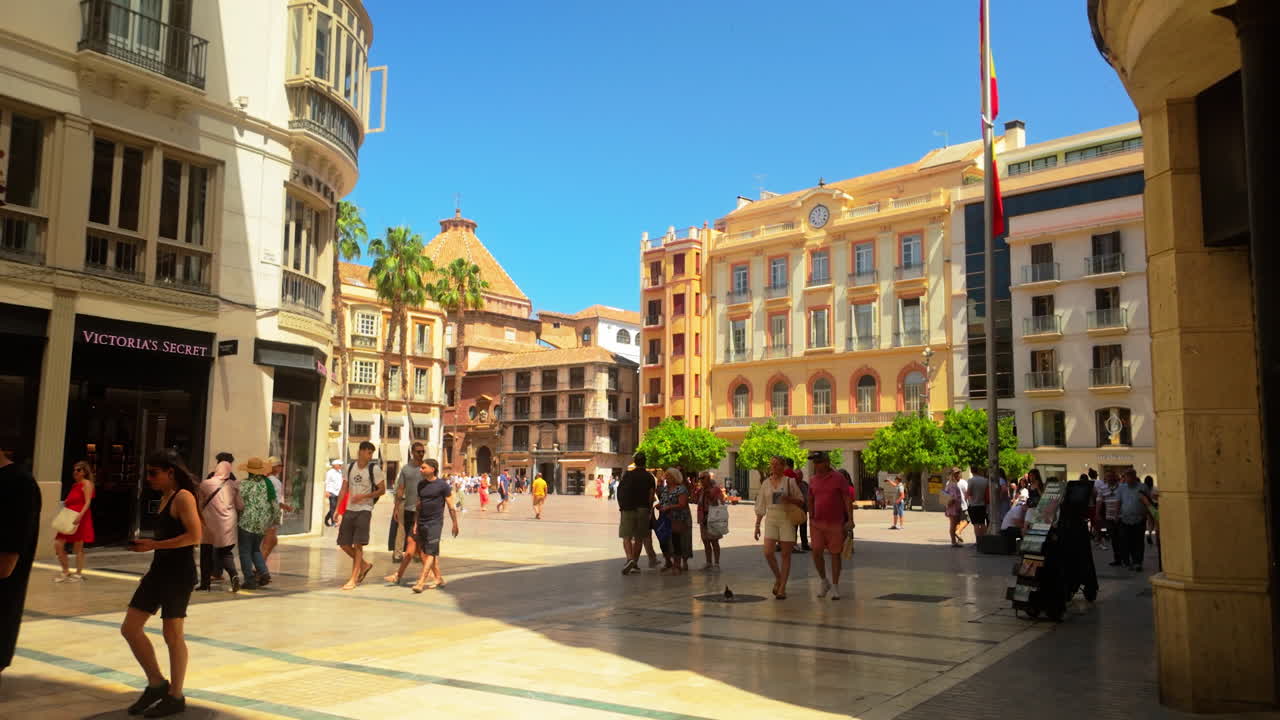 Vibrant street scene in Malaga's historic center with people exploring the charming plaza, surrounded by traditional Spanish architecture and palm trees.