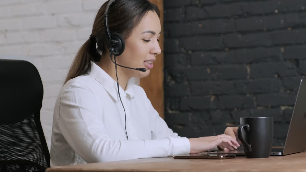 Smiling woman call centre operator, customer support agent wears headset consults client online typing on laptop, talk in internet computer chat, helpline operator secretary make conference video call