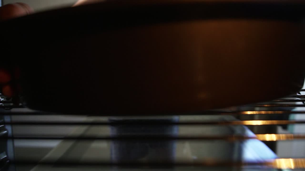 Unrecognizable woman opens the oven's door and puts a baking pan with a cake inside: View from the oven. Beautiful girl in her