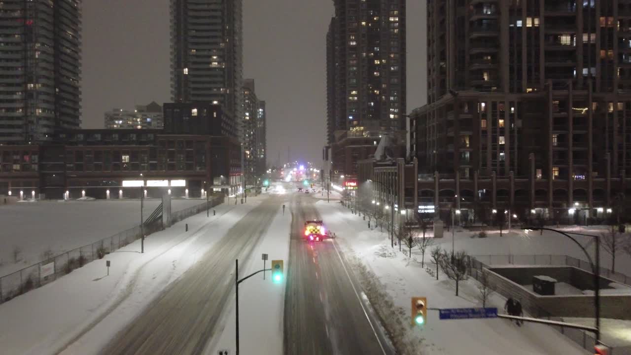 Aerial: fire truck riding in the snowy streets at night with cityscape and lights in Mississauga, Ontario, Canada, establishing drone shot