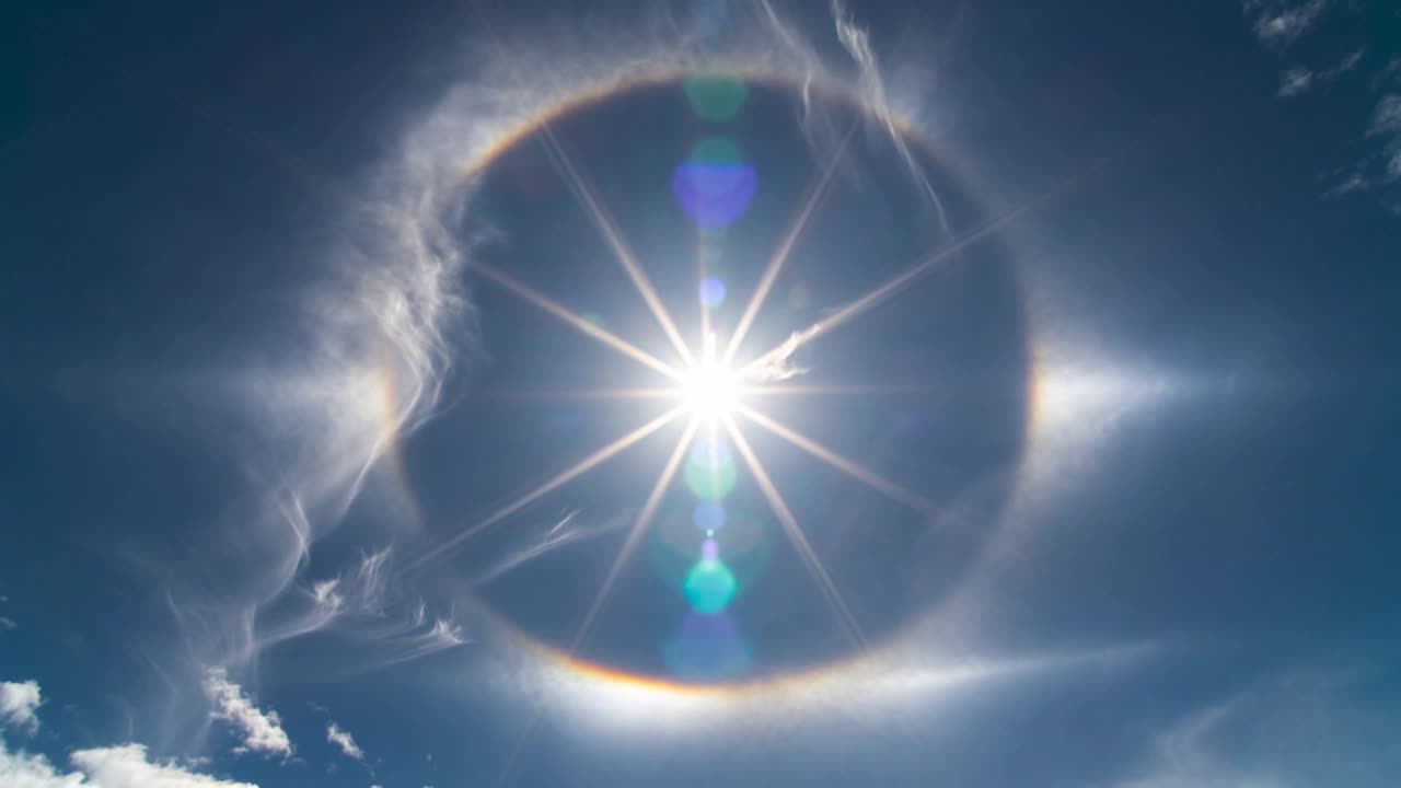 Cirri mutevoli che rivelano il sole con un alone di 22 gradi sopra il cielo di mezzogiorno, alterando il parelio e il lens flare.