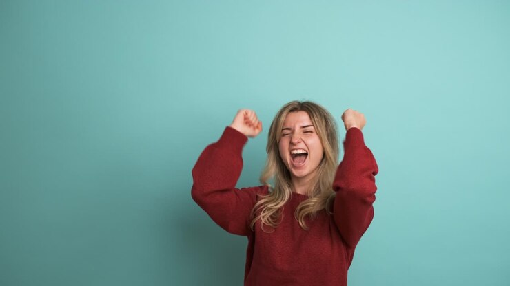 Giovane donna di successo che stringe i pugni in uno studio blu