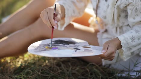 a person painting outdoors with a palette and paintbrush