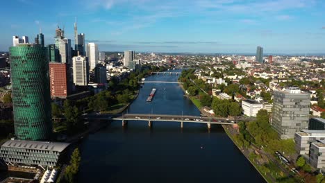 Aerial-dolly-above-Main-river-in-downtown-Frankfurt-Germany-at-midday-as-barge-is-in-transit