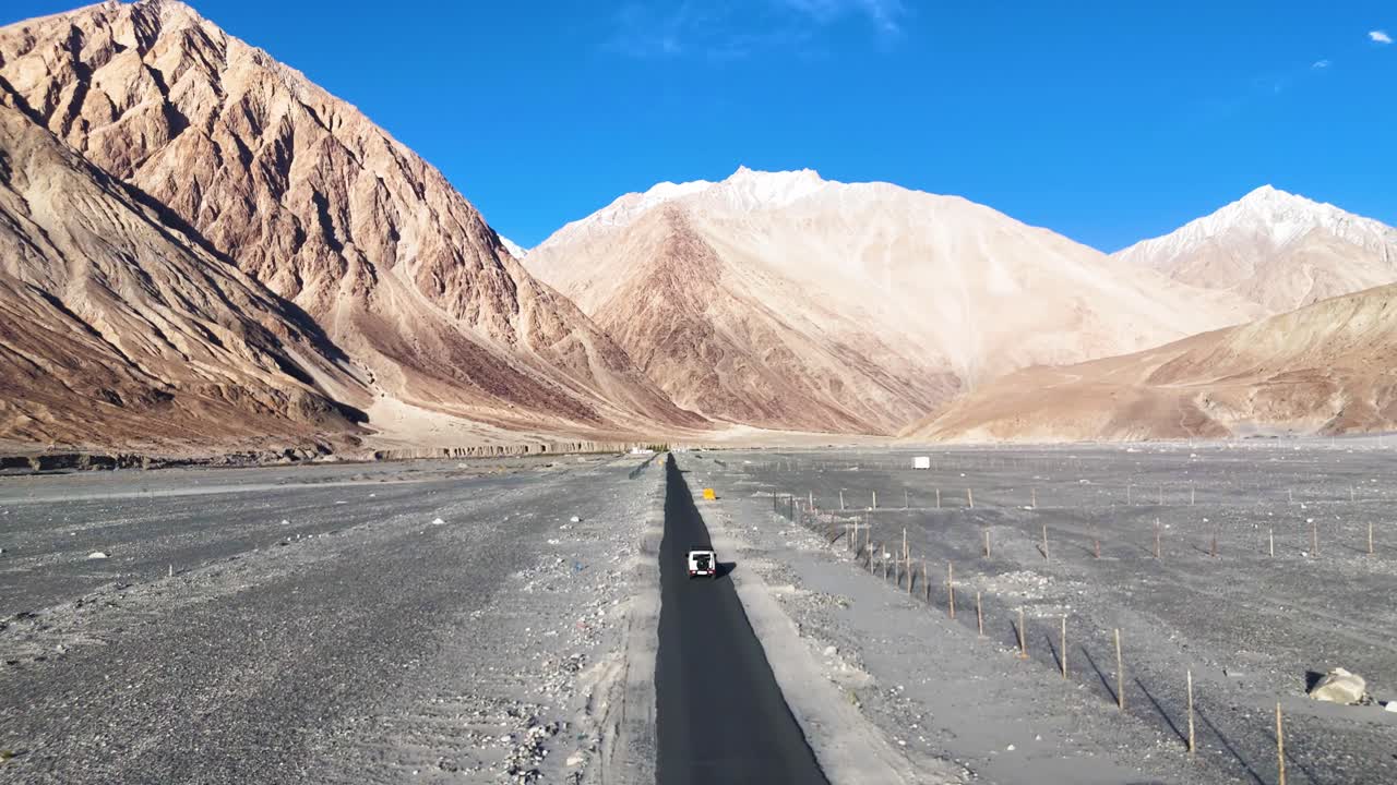 Aerial drone shot of a vehicle moving through Ladakh’s high desert, surrounded by wind-swept hills.