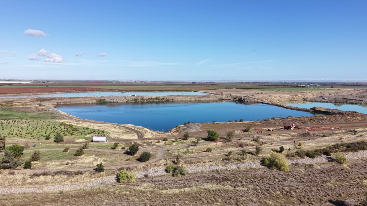 Drone footage moving forward toward a large irrigation pond in Capay Valley, California, surrounded by dry farmland and sparse vegetation under a clear blue sky