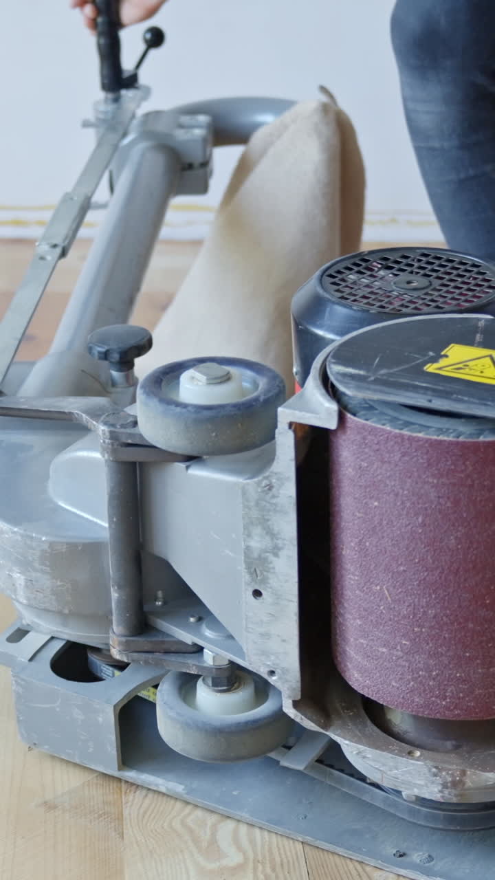 A drum sander with exposed drum as sandpaper is changed for smoothing hardwood floor surfaces.