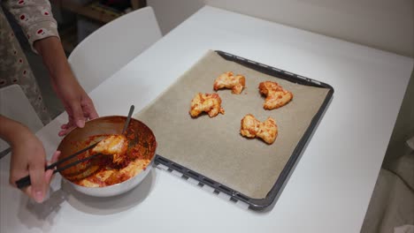 mujer coloca alas de pollo marinadas en una sábana de hornear usando palillos, cocinar almuerzo, cena en casa, comida, hornear, carne, dieta de fitness, preparación de comidas, alimentación saludable, consumo de carne, nutrición, salsa