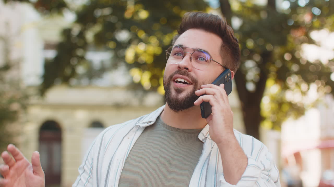 Happy young caucasian man tourist in casual talking on smartphone while standing on city street
