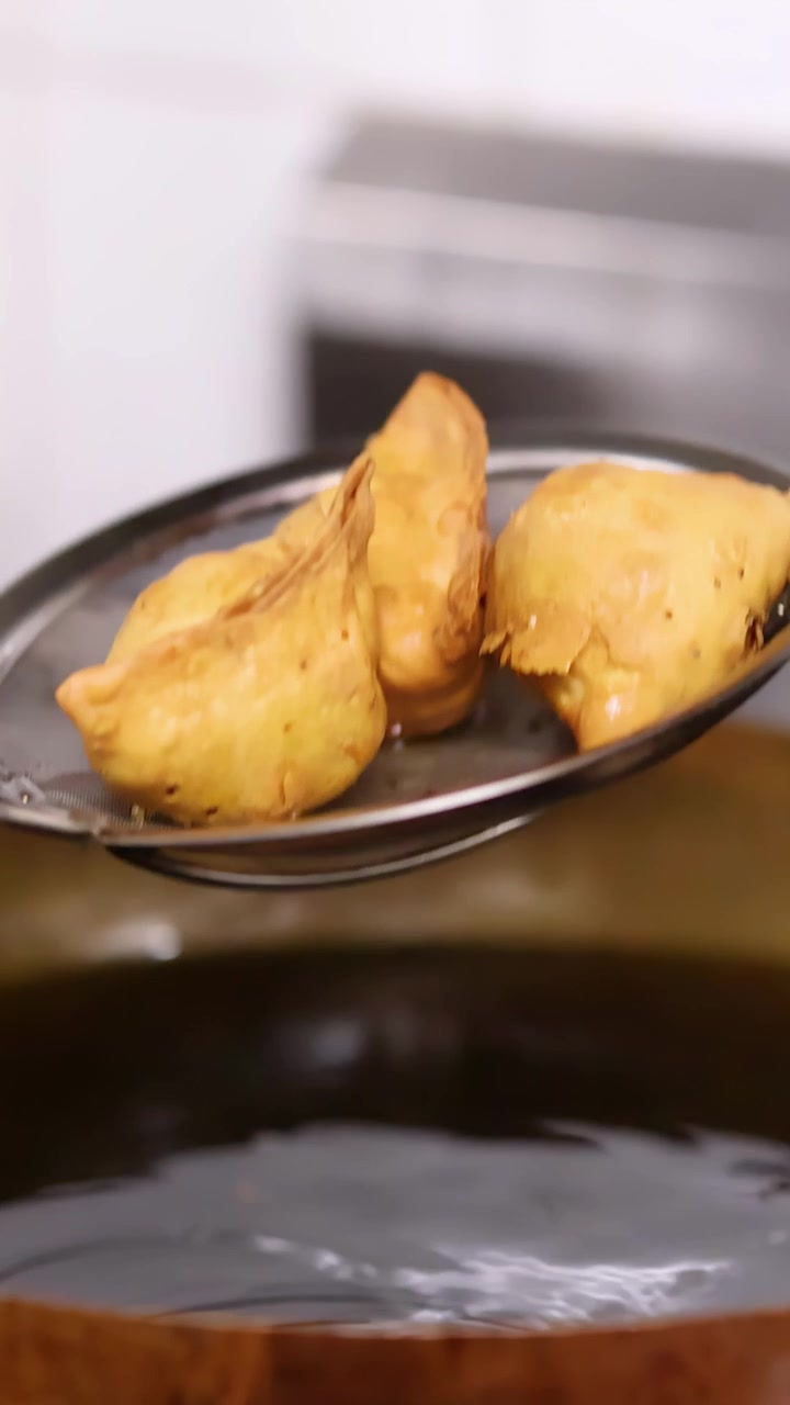 Samosa dorati vengono sollevati dall'olio bollente in un wok di ottone usando una schiumarola di metallo