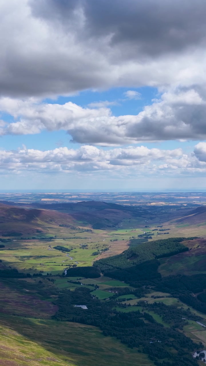 Drone sorvola una suggestiva valle delle Highlands, rivelando colline coperte di erica, fiumi e un cielo nuvoloso spettacolare