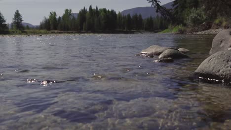 flowing river splashing on a riverbank shore with mountains in the background