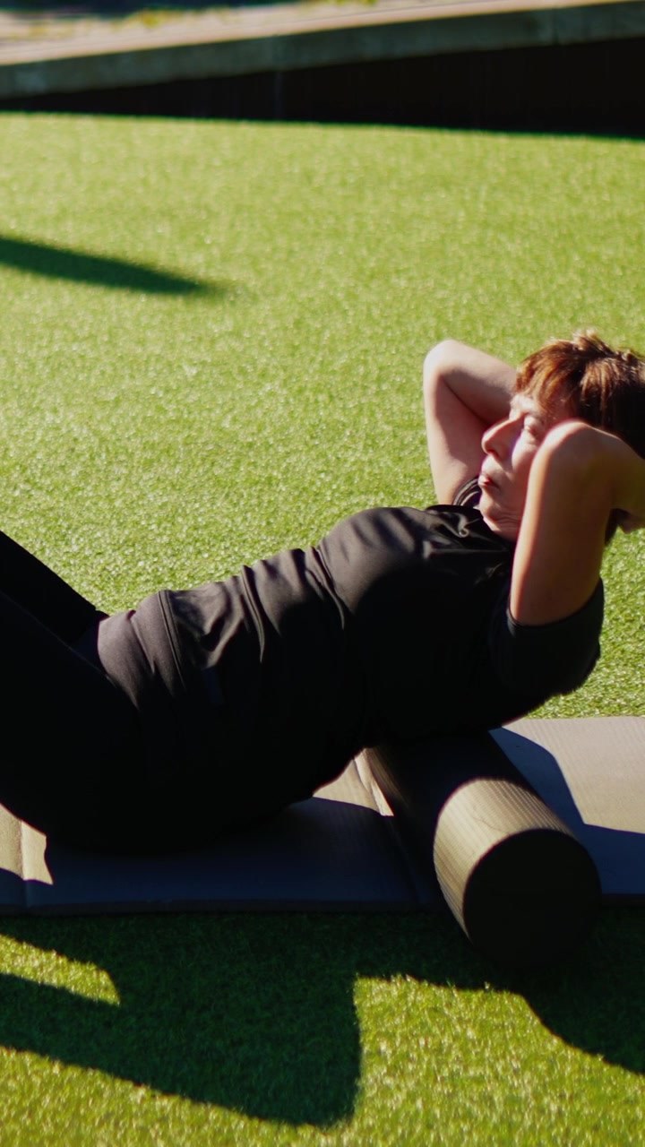 Donna che utilizza un foam roller per lo stretching della schiena su erba artificiale