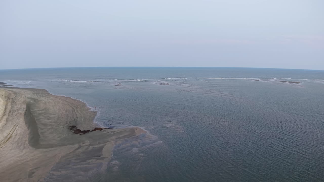 Aerial drone footage of Charleston, South Carolina capturing a sandy peninsula extending into calm blue water, with a wide river or bay and a distant horizon on a hazy day