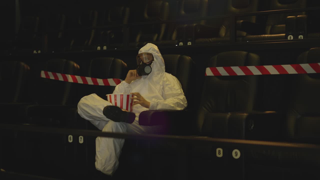 영화관 에서 혼자 앉아 팝콘 을 먹고 있는  ⁇ 색 보호 의상 과 호흡기 를 입은 남자 의 초상화