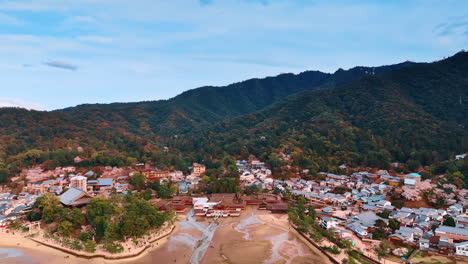 thick forests cover the rocks near the inhabited area at the island of miyajima, japan. drone footage above the spectacular itsukushima shrine at low tide.