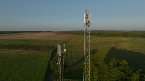 Two-cellular-towers-in-the-middle-of-farmland-during-sunrise,-aerial-orbital-closeup