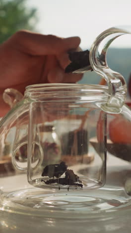 hombre transfiere el té a la tetera con cuchara. joven arregla accesorios de té preparando el escenario para una ceremonia sincera. desayuno saludable por la ventana