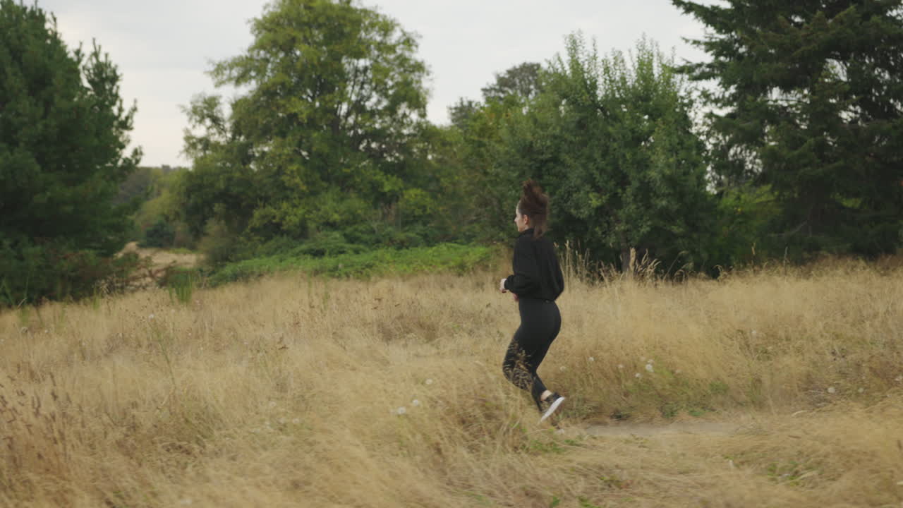Young attractive athletic white female in all black clothing jogging through a field on a gloomy gray day
