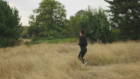 young attractive athletic white female in all black clothing jogging through a field on a gloomy gray day