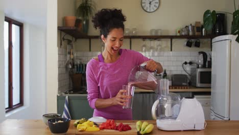 retrato de una mujer de raza mixta vertiendo jugo de fruta en un vaso de un fabricante de jugo en la cocina en casa