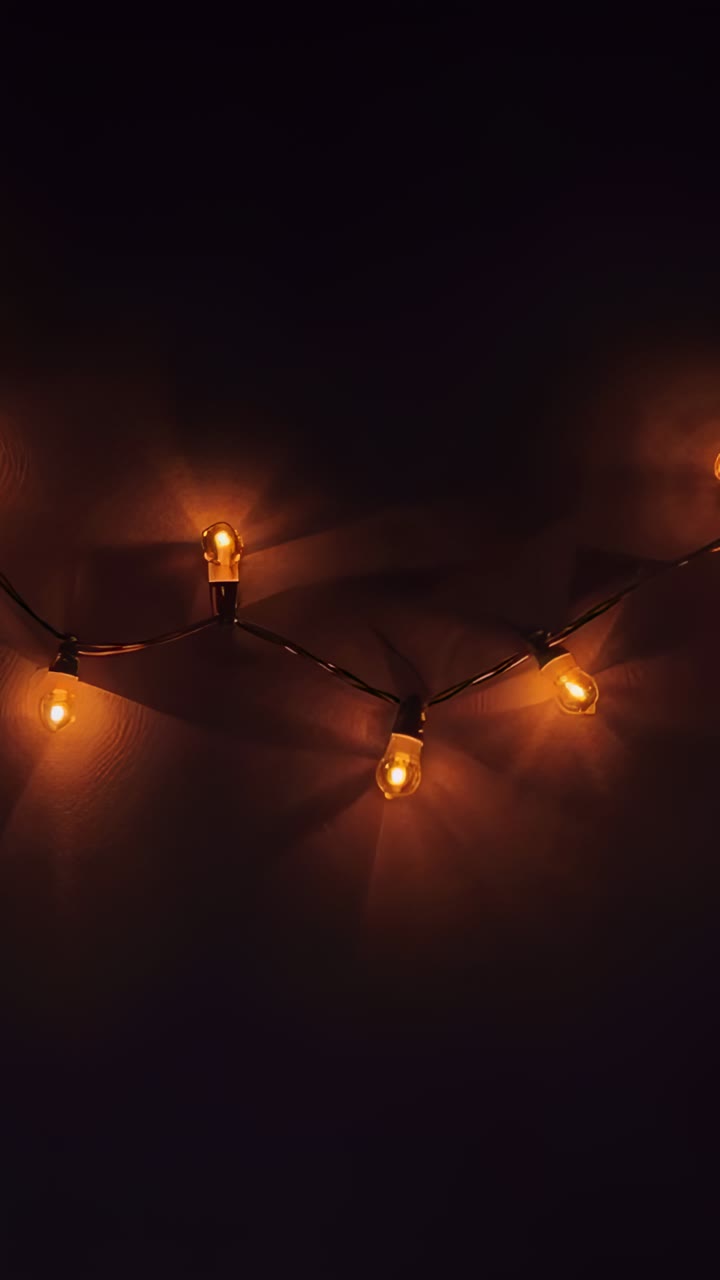 Video verticale: lampadine ambrate tremolanti e filo appeso alla parete di casa, corrente che alimenta una calda illuminazione