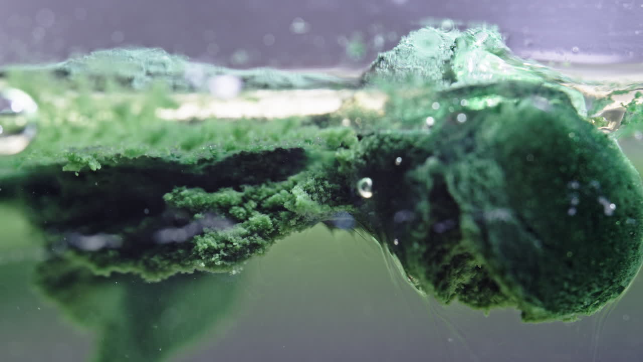 Dissolving green pill in water with bubbles and foam forming on the surface