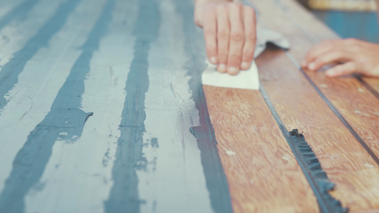 나무 보트의 목재 지붕을 밀봉한 후 마스킹 테이프를 제거하는 남성 손