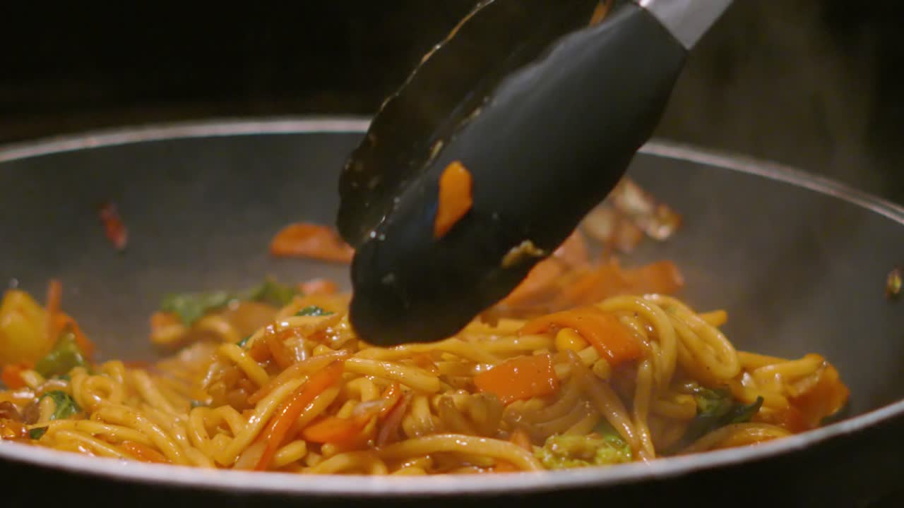 la mano de la mujer agarrando y retorciendo fideos fritos con verduras mientras el vapor caliente se eleva en cámara lenta. imágenes de comida slomo 4k.