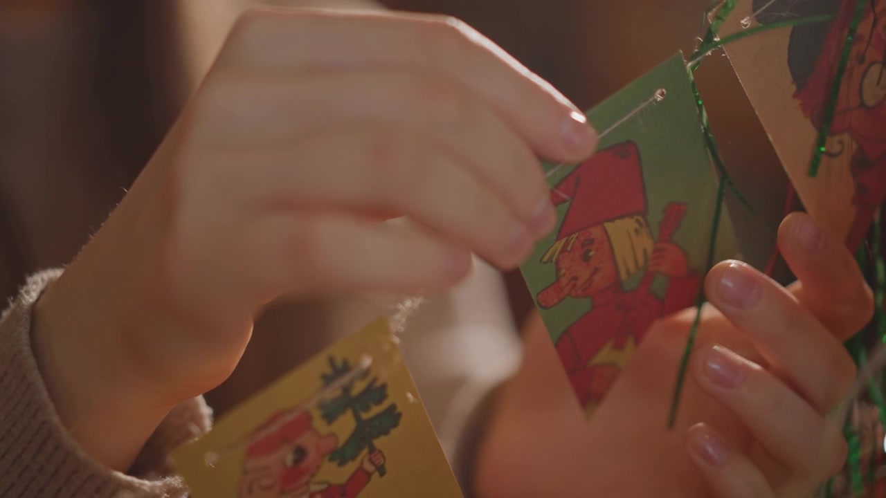 Close-up de mãos arrumando cartões vintage. Dedos delicadamente enfiando cartões de papel nostálgicos sob luz suave. Cenário aconchegante onde as mãos prendem cuidadosamente cartões retrô a um cordão decorativo festivo