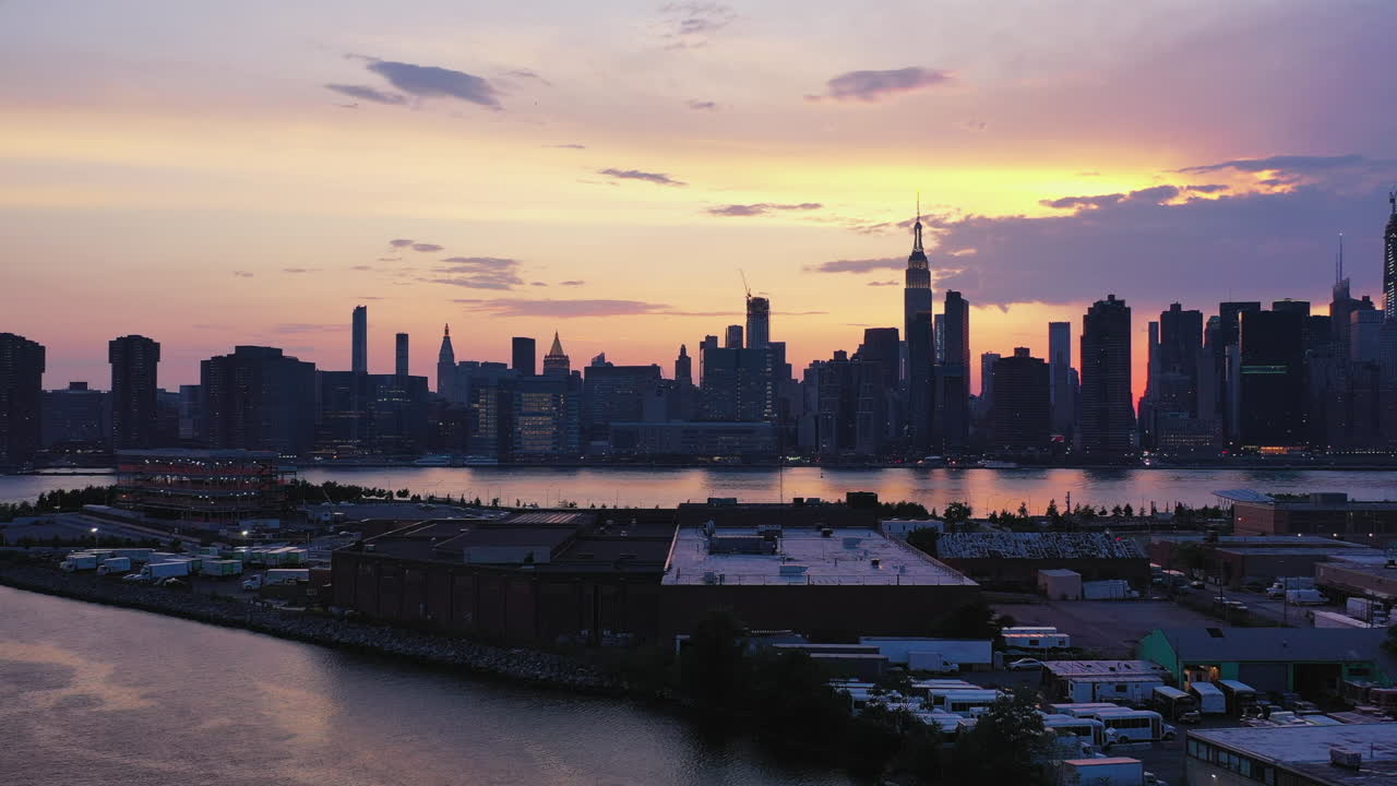 극적인 공중 드론 카메라가 물러납니다 - 뉴욕시의 동쪽을 배경으로 물 위로 들어 올려집니다 - 보라색 일몰 하늘