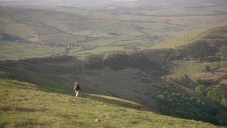 dolly lateral de mano de una joven rubia con mochila caminando por el lado de mam tor, castleton, peak district, inglaterra al atardecer