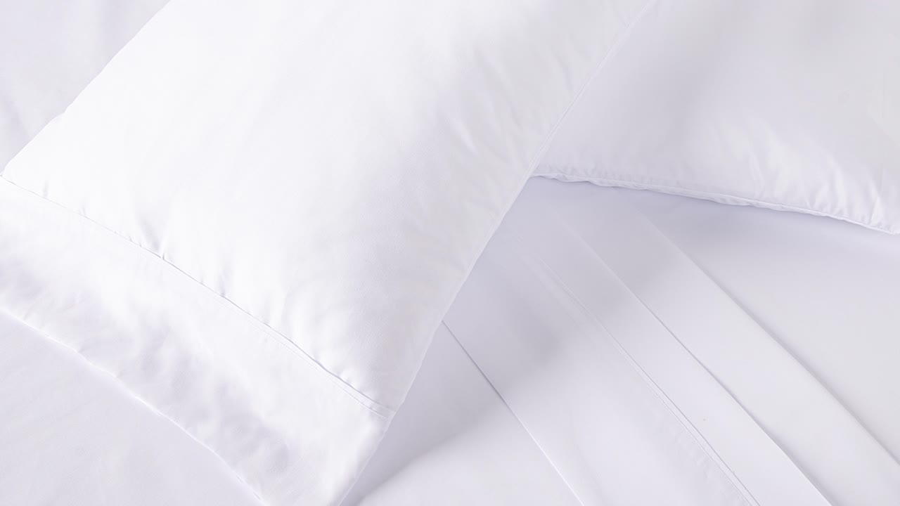Camera slowly zooms into fresh white bedding in soft morning light