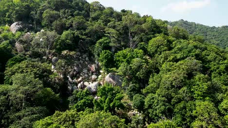 Large-rock-formation-and-seaside-cabins-with-Long-boats-on-an-inlet-in-Mango-Bay,-Ko-Tao-Island-Thailand,-Aerial-pull-out-shot