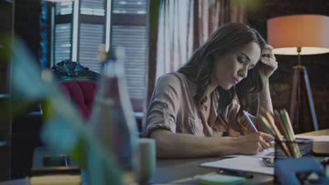 Concentrated-businesswoman-making-notes-at-table-with-laptop-in-office