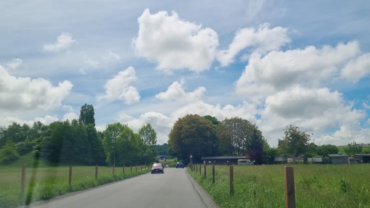 From a passenger’s perspective in a moving car, the tranquil rural landscape near Bern, Switzerland, glides past beneath a partly cloudy sky, reflecting the calm pace of country life