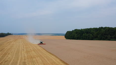 approaching combine harvester in the ripe barley field. heavy smoke produced by the machine. farmlands and forests at the backdrop.