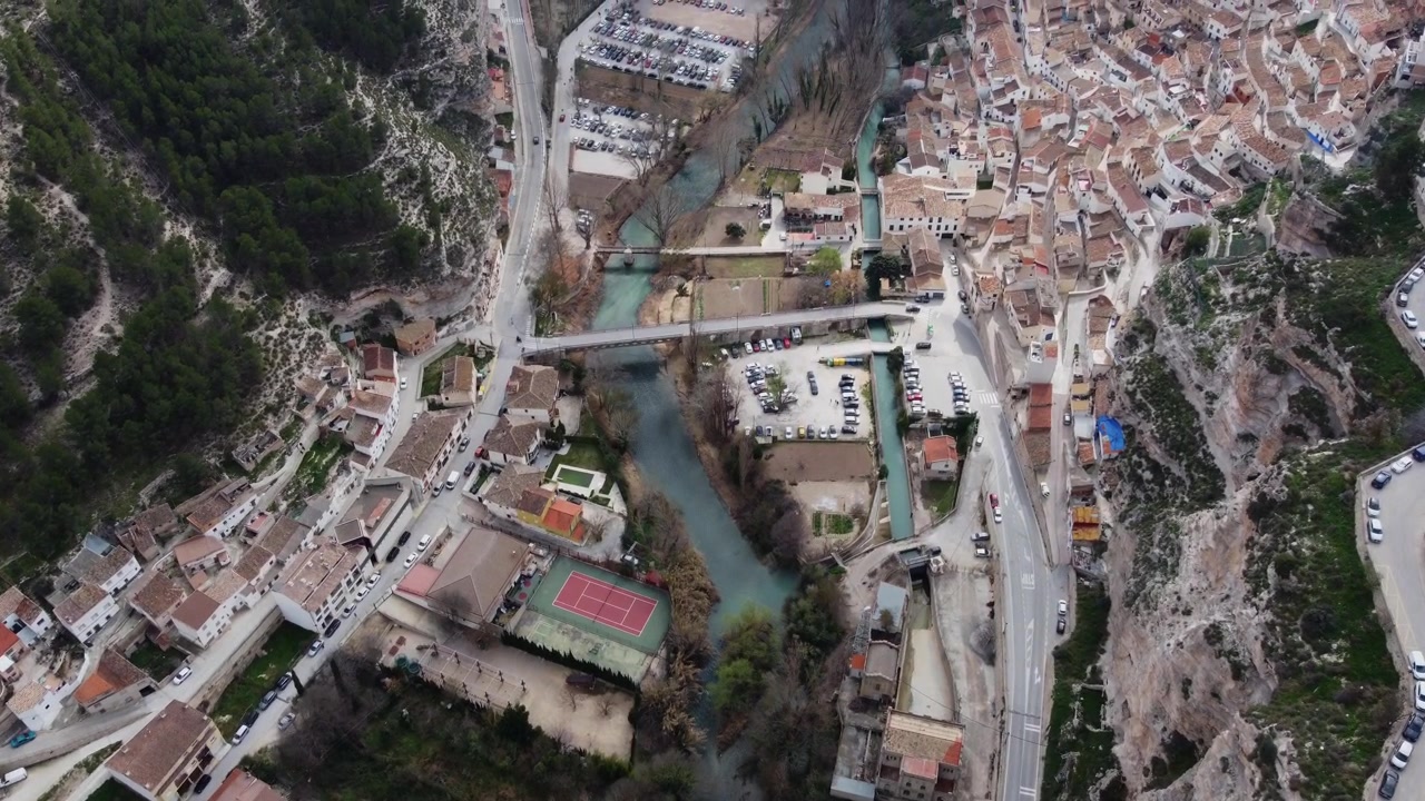 Vuelo de dron aéreo 4K sobre Alcalá del Júcar, España. Perspectiva de gran angular que muestra la parte baja del pueblo y el río Júcar en el fondo del desfiladero