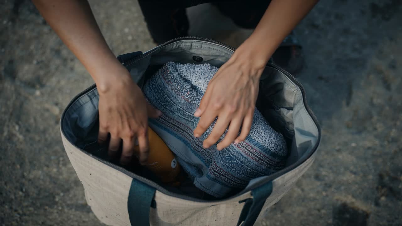 Starting with folded towel inside tote, hands sliding yellow bottle beside towel for beach trip