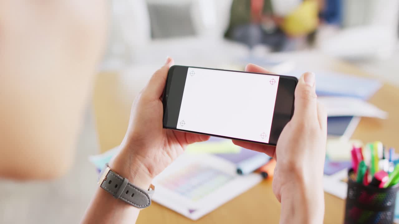 아시아 여성이 스마트폰으로 비디오 통화를 하고, 화면에 공간을 복사하고, 동료들이 뒤에 있고, 느린 동작입니다.