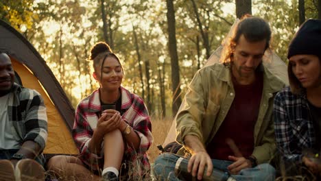 Close-up-shot-of-a-happy-group-of-people-on-a-hike-in-plaid-shirts-and-hiking-clothes-pouring-tea-into-glasses-against-the-backdrop-of-a-sunny-summer-forest.-Using-a-thermos-during-a-halt-against-the-backdrop-of-tents