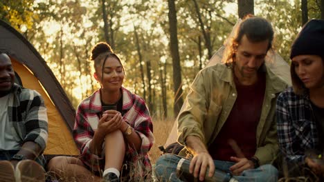 toma de primer plano de un grupo feliz de personas en una caminata en camisas a cuadros y ropa de senderismo vertiendo té en vasos contra el telón de fondo de un bosque de verano soleado. usando un termo durante una parada contra el fondo de tiendas de campaña