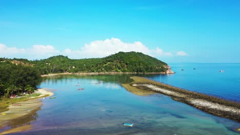 fishing boats anchoring on calm lagoon protected by corals and rocky barrier reflecting green hills coastline in thailand