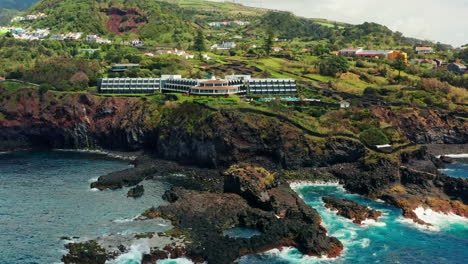 cinematic aerial drone shot of a beautiful resort located on top rocky coastline in sao miguel island, azores - portugal