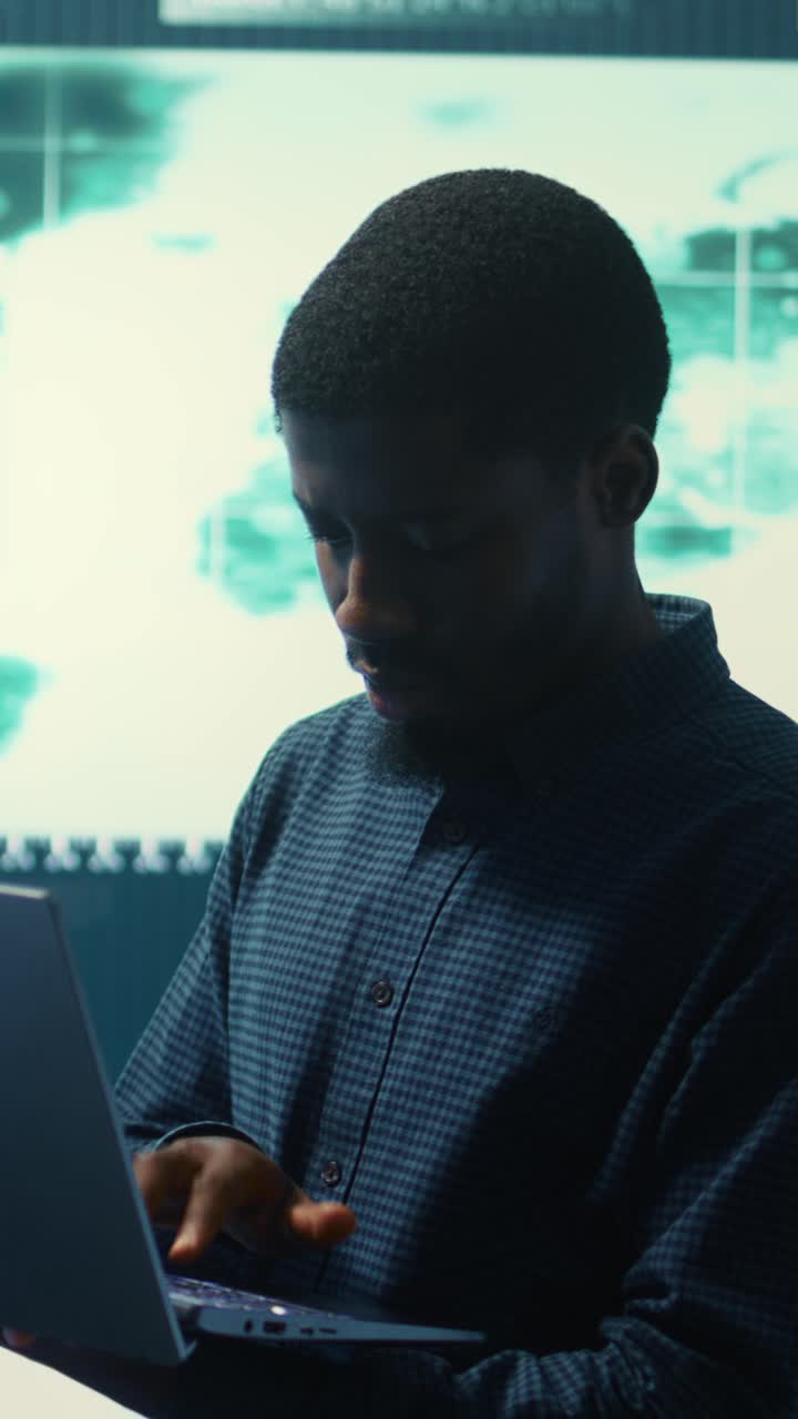 Young African American Man Working on Laptop in High-Tech Control Room