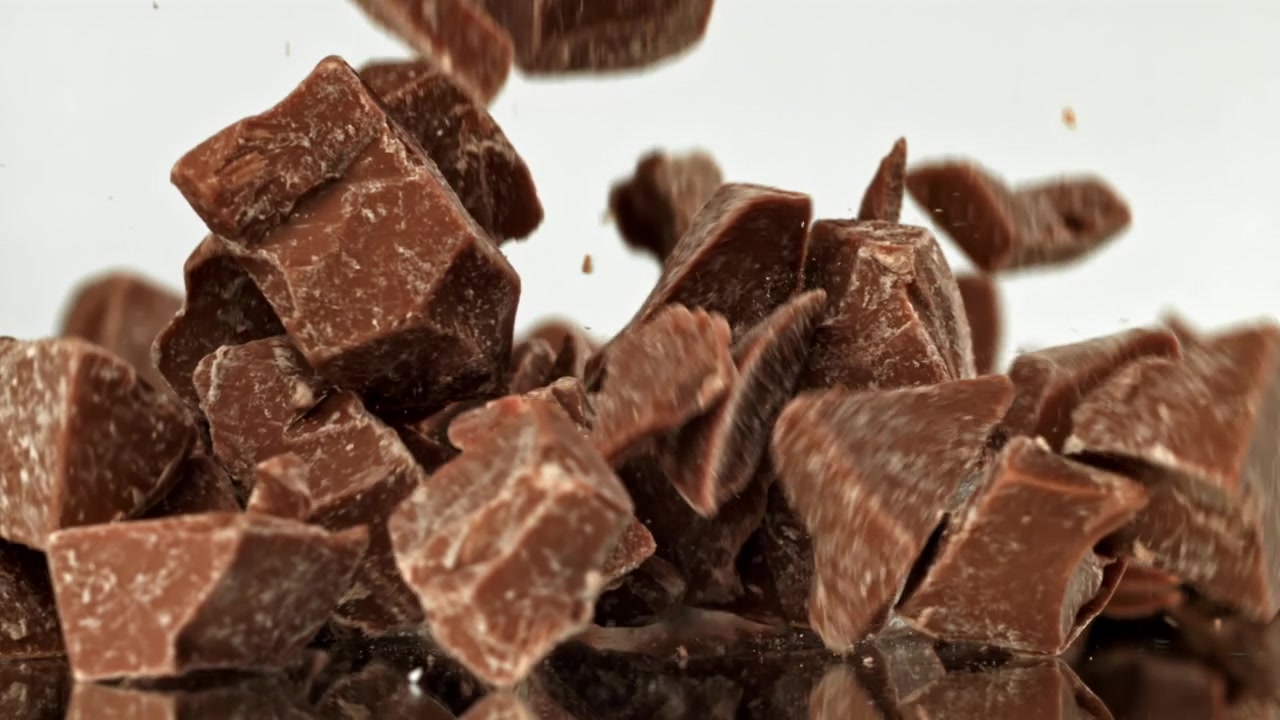 Pezzi di cioccolato che cadono al rallentatore su una superficie riflettente