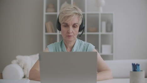 aged woman is communicating online using laptop with internet and headphones with microphone online chat tech support