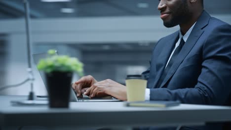 360 degree office: happy successful black businessman sitting at desk using laptop computer. african american entrepreneur in suit working with stock market investing. moving around tracking shot