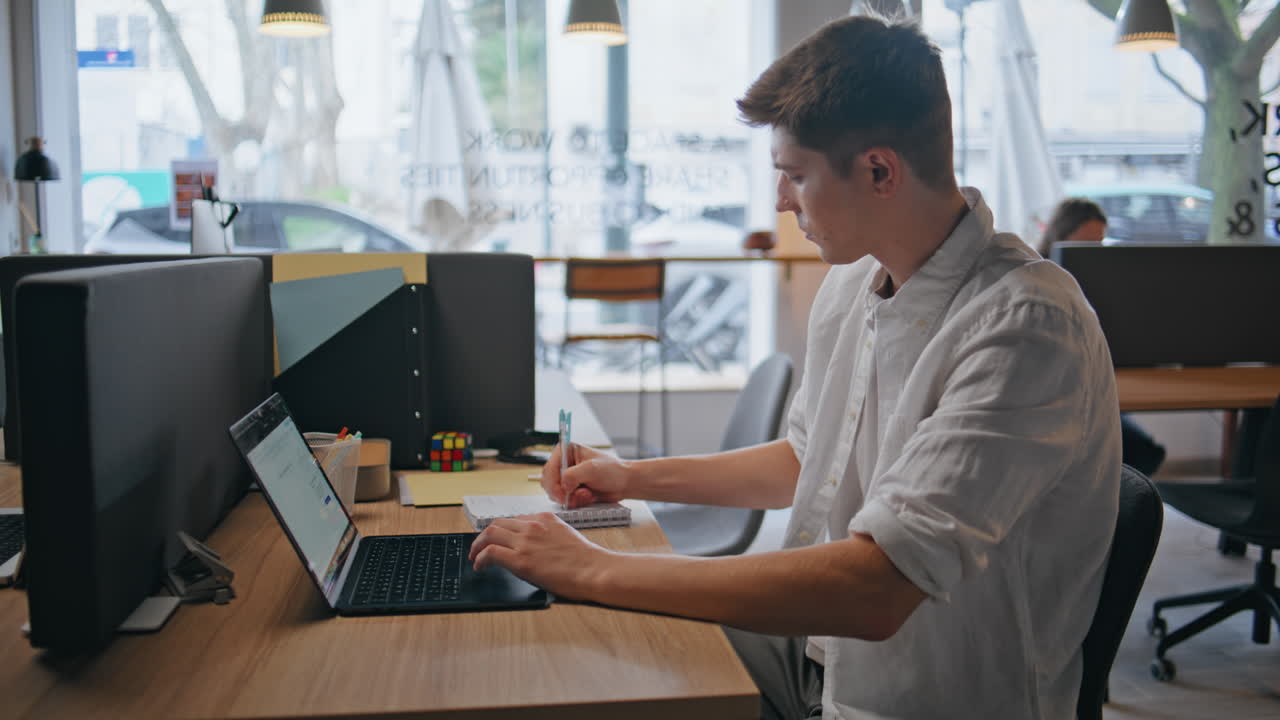 Thoughtful creator staring laptop in office interior closeup. Man writing notes
