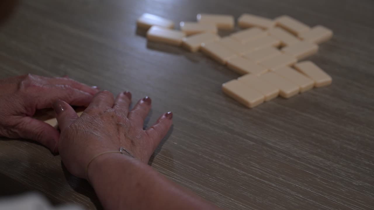 ciudadana anciana con las manos agarrando dominós después de que se mezclan